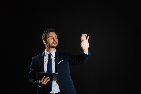 Point of vision. Concentrated handsome unshaken man holding the tablet holding hand up and touching to invisible object.の写真素材