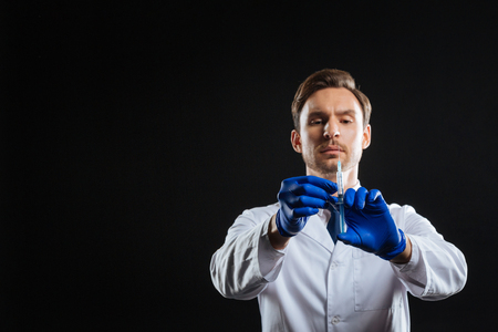 Full concentration. Careful calm skilled doctor standing in the empty room holding and dosing a syringe.の写真素材