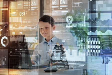 Diligent boy. Cheerful clever little boy smiling and looking attentively at the screen of a modern laptop while touching a wonderful modern inventionの写真素材