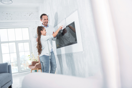 Futuristic apartment. Nice joyful positive father and daughter standing together and using the control panel while being at homeの写真素材