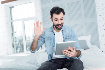 Hey you. Happy freelancer opening mouth while looking at his gadget, sitting on his bedの写真素材