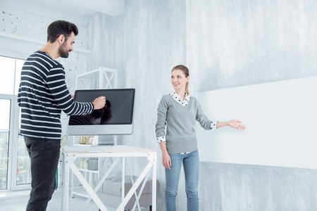 Turn on computer. Charming female person expressing positivity while pointing at wall and looking asideの写真素材