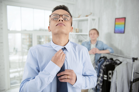 Everything perfect. Meditative earnest focused man touching tie while wearing glasses and looking upの写真素材