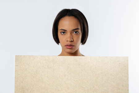 Social event. Portrait of a nice pleasant young woman standing against white background and holding a sign while participating in the protestの写真素材