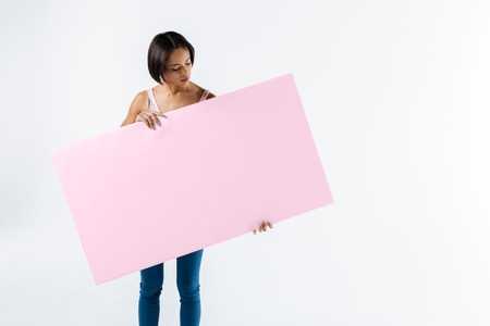 Young activist. Smart serious young woman holding a pink poster and looking at it while standing against white backgroundの写真素材