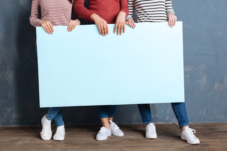Female slogan. Close up of a big blue poster being in hands of joyful nice women while showing their sloganの写真素材