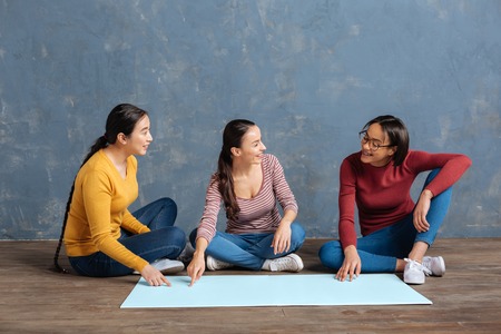 Informal atmosphere. Cheerful happy nice women sitting on the floor and talking to each other while discussing their ideasの写真素材