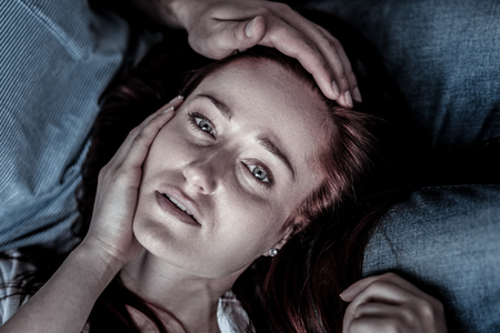 Serious illness. Frustrated depressed sad woman lying on knees of her husband feeling bad herself and touching her face.の写真素材