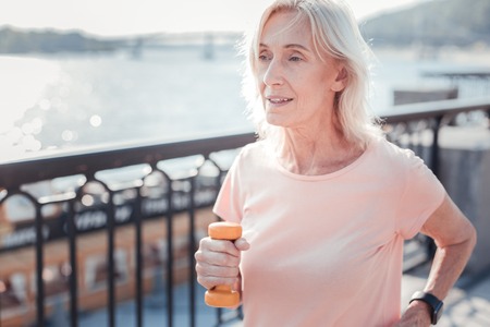 Air and sport. Pleasant aged confident woman holding dumbbells having training and running across the quay.の写真素材