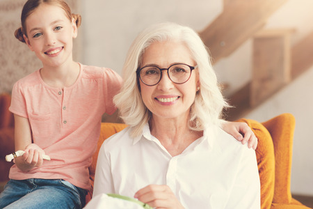 Happy delighted elderly woman looking at you and smiling while doing her favourite hobbyの写真素材