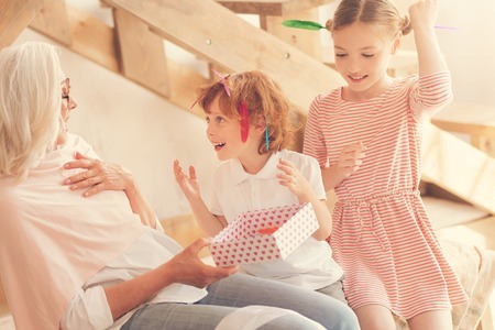 Nice pleasant aged woman holding a gift box and looking at her grandson while being surprised