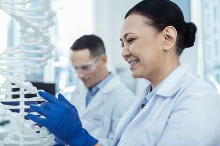 Study evolution. Positive asian woman workign in a lab with her colleague while studying dna model