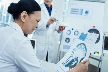 Check it up. Nice asian female doctor holding brain image while thinking out future surgeryの写真素材