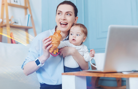 Tasty dessert. Happy delighted pretty woman smiling and holding a croissant while intending to eat itの写真素材