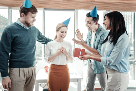 Happy birthday. Attentive funny friendly colleagues standing in the office congratulating their...