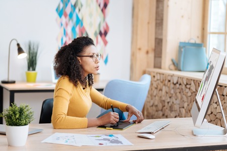 Concentration. Good-looking concentrated young curly-haired woman working on her laptop while...