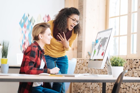 Unbelievable. Pretty delighted young smart women working in the office and looking at the screen while discussing their new projectの写真素材