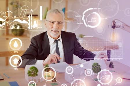 Positive worker. Positive emotional experienced architect smiling while working with miniatures in his comfortable officeの写真素材