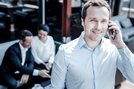 Business call. Delighted good looking positive man holding his smartphone and smiling while making a business callの写真素材