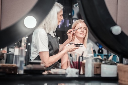 My workplace. Experienced nice makeup artist holding makeup brushes and applying cosmetics while workingの写真素材