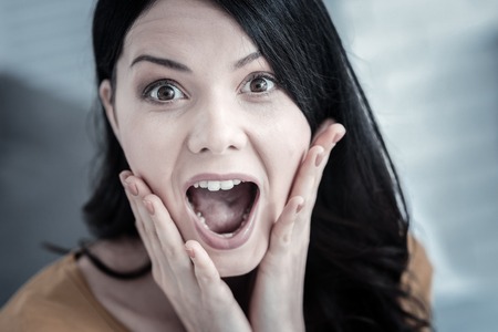 Expression of surprise. Portrait of a positive emotional young woman holding her cheeks and opening the mouth while expressing her surpriseの写真素材