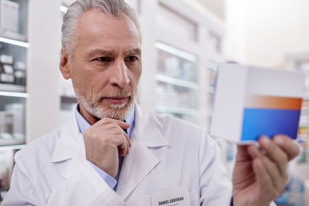 Right dosage. Senior attentive male pharmacist touching chin while rising medicationの写真素材