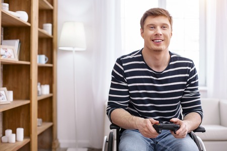 Be positive. Cheerful male person expressing positivity while holding playing console in both handsの写真素材