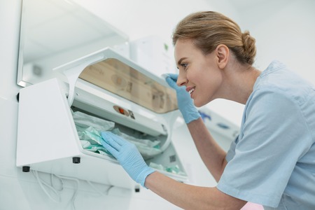 I love cleanness. Joyful skilled dentist smiling and sterilizing her instrumentsの写真素材