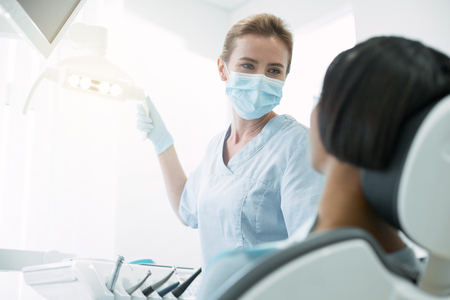 Fixing teeth. Joyful skilled dentist wearing a mask and starting doing dental workの写真素材