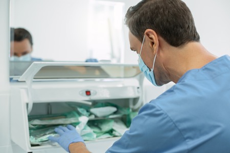 My dental office. Concentrated dark-haired dentist wearing a uniform and sterilizing instrumentsの写真素材