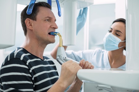 Modern device. Nice concentrated man opening his mouth and having a dental device in itの写真素材