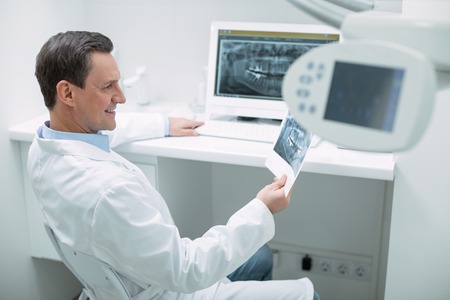 Great results. Smiling experienced dentist holding an image and working on her advanced deviceの写真素材