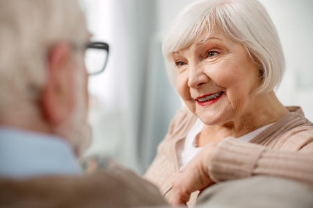Pleasant mood. Portrait of a delighted aged woman sitting together with her husband on the sofa