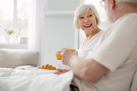 Delicious meal. Joyful positive aged couple having breakfast while lying in bed