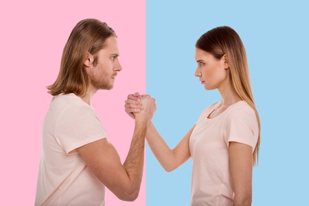 Equal strength. Handsome young man and a woman being focused on an arm-wrestling and staring at each...