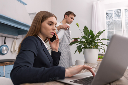 Seriousness. Serious determined woman discussing work on the phone and her husband keeping houseの写真素材
