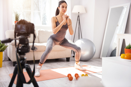 Aspiring vlogger. Athletic young woman doing squats and recording her exercises complex on cameraの写真素材