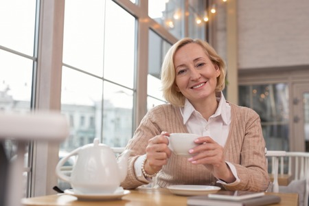 Pleasant day. Charming blond woman sitting in a cafe and drinking teaの写真素材