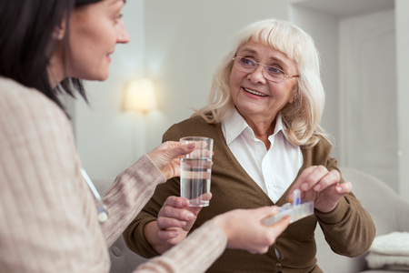 Individual treatment. Happy senior woman taking pills from nurse while smilingの写真素材