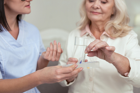 Daily dosage. Close up of senior female hands receiving drugs from female hands that carrying containerの写真素材