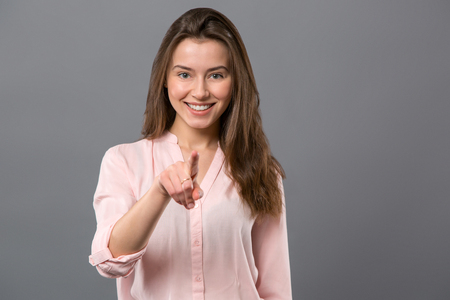 Friendly look. Pleasant young woman smiling to you while pointing with her fingerの写真素材