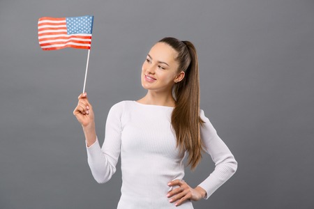 Pleasant young woman holding US flag while showing her patriotic feelingの写真素材