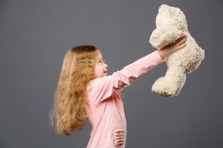 Pleasant cheerful girl looking at her bear while holding it in front of herの写真素材