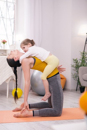 Healthcare. Concentrated muscular mother doing some exercises with her daughter while training at homeの写真素材
