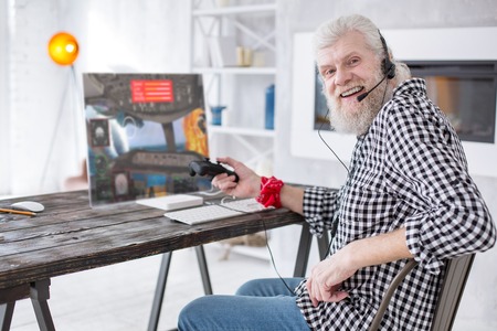Favorite game. Joyful elderly man posing for the camera and smiling while taking a break at playing an multiplayer online aircraft battle simulatorの写真素材