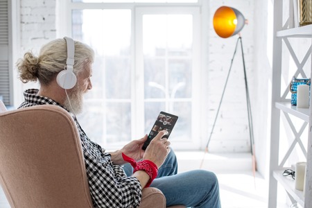 Nice music collection. Pleasant elderly man sitting comfortably in his armchair and choosing a track...