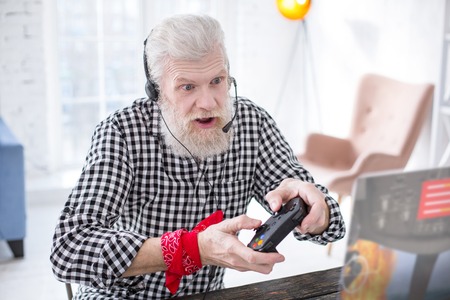 Gaming enthusiast. Charming elderly man playing a multiplayer online video game and excitingly...