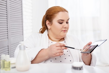 Makeup artist. Inspired stout woman wearing a bathrobe and applying make-upの写真素材
