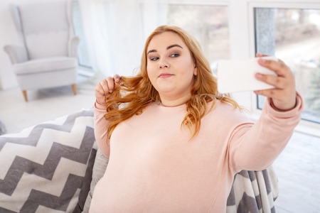 Delighted stout woman relaxing at home and taking selfiesの写真素材