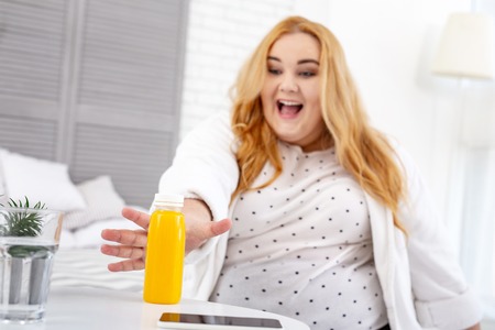 Joyful overweight woman smiling and taking her juiceの写真素材